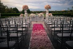 an outdoor ceremony setup with white chairs and pink flowers on the aisle leading up to it