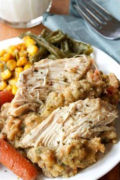 a white plate topped with meat covered in gravy next to green beans and corn