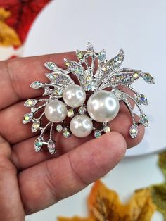 Add a touch of elegance to any outfit with this stunning Rhinestone Crystal and Pearl Flower Brooch Pin. The shining rhinestone crystals catch the light beautifully, reflecting different colors depending on the angle and creating a dazzling effect.  The brooch also features lustrous pearls and delicate flower petals made from high-quality materials, adding to its vintage-inspired charm. Measuring approximately 5.5cm in diameter, this brooch is the perfect size to wear on your lapel, blouse, dress, or scarf. Its silver color complements any outfit, making it ideal for special occasions such as weddings, engagements, parties, or evening wear. This Elegant Rhinestone Crystal and Pearl Flower Brooch Pin is not only a beautiful accessory for yourself but also makes a great Mother's Day gift for White Crystal Wedding Brooches, White Crystal Brooches For Wedding, Elegant Crystal Embellished Brooches For Wedding, Elegant Crystal-embellished Wedding Brooches, Wedding Crystal Brooches With Sparkling Stones, Elegant Crystal-embellished Brooches For Weddings, Crystal Flower Brooch For Weddings, White Crystal Brooch With Rhinestones, Wedding Silver Brooches With Sparkling Stones