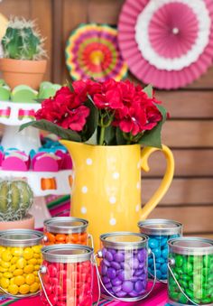 colorful candy jars with flowers in them are on a table next to plates and cups