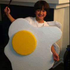 a young boy dressed up as an egg and holding a frying pan on his chest