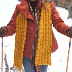 a woman in red jacket holding two ski poles and wearing yellow scarf on snow covered ground