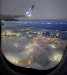 the view from an airplane window shows clouds and lights in the distance, as seen from above