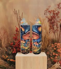 two tall vases sitting on top of a wooden block in front of some flowers