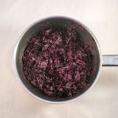 red cabbage cooking in a pot with a spoon on the side and white tablecloth behind it