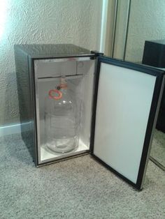 an empty glass bottle in a black box on the floor next to a mirror with its lid open