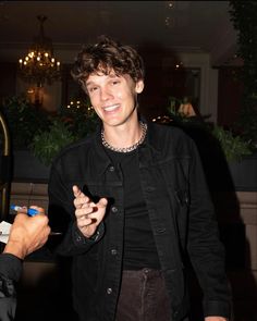 a man in black jacket talking to another person holding a cell phone and pointing at it