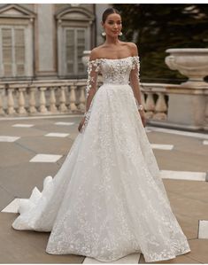 a woman in a white wedding dress standing on a stone walkway with an ornate building behind her