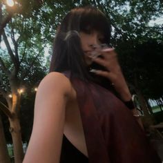 a woman with long black hair is talking on her cell phone while standing in front of some trees