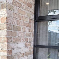 a cat sitting on the window sill of a brick building looking out at the street