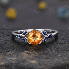 a ring with an orange stone surrounded by blue sapphires on top of a rock