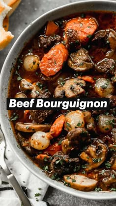 a white bowl filled with stew and carrots on top of a table next to bread