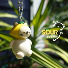 a cat keychain hanging from a plant with the words sour kitty on it