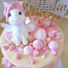 a birthday cake decorated with pink and white icing, seashells and a unicorn figurine