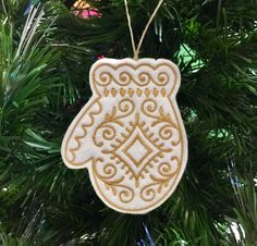 an ornament hanging from a christmas tree decorated with gold and white designs on it