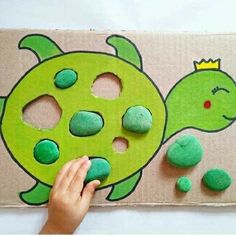 a child's hand is painting a turtle on a cardboard board with green rocks