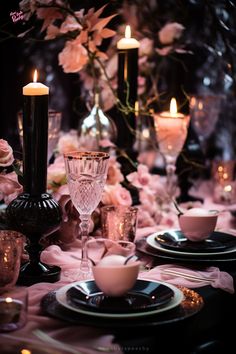 the table is set with black and white plates, silverware, candles and pink flowers