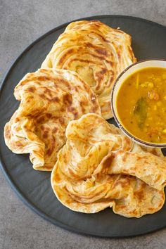 some food is on a black plate with a bowl of soup and two pita breads