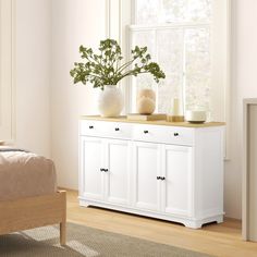 a white dresser with flowers and candles on it in a bedroom area next to a bed