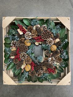 a christmas wreath made out of pine cones, berries and evergreen leaves on a wooden box