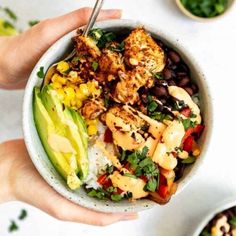 two hands holding a bowl filled with chicken, rice and avocado next to other bowls