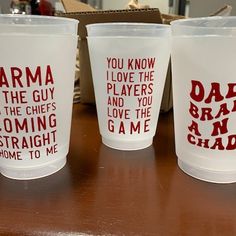 three plastic cups with words on them sitting on a wooden table next to a box