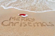 a santa hat is written in the sand at the beach with merry christmas written on it