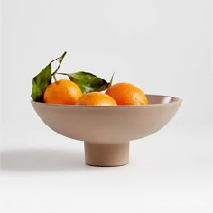 three oranges in a bowl with green leaves