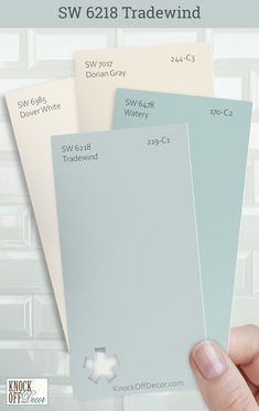 a hand holding three different shades of paint in front of a white tile wall with the words sw 618 tradewind on it