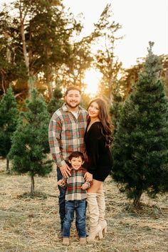 a man and woman pose with their son in front of christmas trees