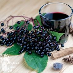 a glass of wine next to some black berries and anisette on a wooden table