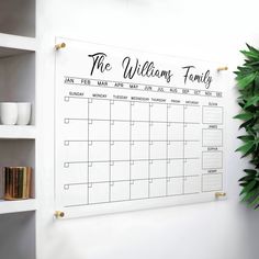 a white wall mounted calendar with the words, the welcome family on it next to a potted plant