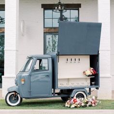 an old truck is parked in front of a building with flowers on the bed and side