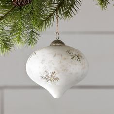 a white christmas ornament hanging from a pine tree with snowflakes on it