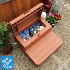 an open storage box sitting on the ground next to some flowers and potted plants