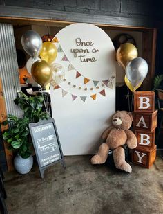 a teddy bear sitting in front of a sign and balloons