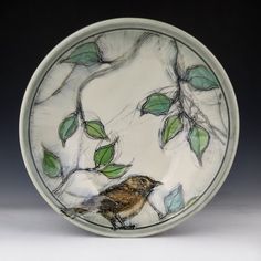 a plate with a bird sitting on it's side and green leaves around the edge