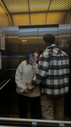 a man and woman standing in an elevator looking at their cell phones while taking pictures