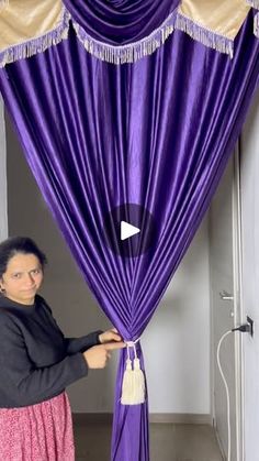 a woman standing in front of a purple curtain with tassels on the top