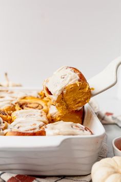 a white casserole dish filled with cinnamon rolls and cream cheese frosting on top