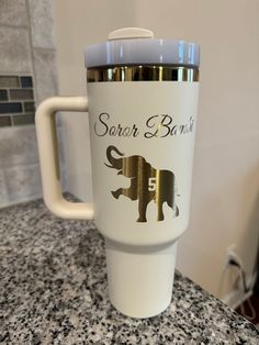 a white and gold travel mug sitting on top of a granite countertop next to a wall