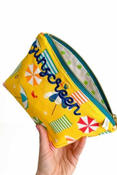 a person holding up a yellow zippered pouch with an umbrella pattern on the front