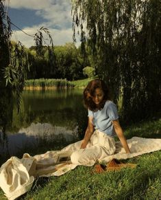 a woman sitting on top of a blanket next to a lake