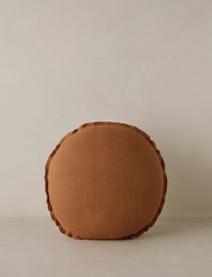 a round cushion with braided edges on a plain surface, in light brown color