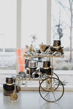 a cart with cups on it in front of a window next to a vase and other items