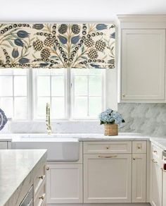 a kitchen with marble counter tops and white cabinets, blue flowers in a basket on the window sill