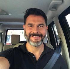 a man with a beard and black shirt taking a selfie in the back seat of a car