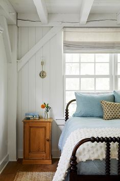 a bed sitting under a window next to a wooden dresser in a white walled room