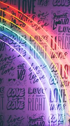 the word love is written in different languages on a wall with a rainbow colored light