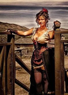 a woman dressed in steampunk clothing standing on a wooden fence with her arms outstretched